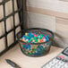 A black Universal jumbo mesh storage dish full of colorful push pins and a calculator.