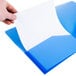 A person's hand holding a white sheet of paper in a translucent blue Avery folder.