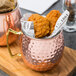 Two American Metalcraft hammered copper Moscow Mule mugs with a cocktail inside.