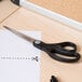 Universal stainless steel scissors with black bent handles on a piece of paper on a table.
