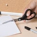 A hand using Universal stainless steel scissors with black bent handles to cut paper.
