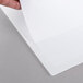 A person's hand using a Universal white economy binder to hold a piece of paper.