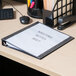 A black Universal Deluxe Non-Stick View Binder on a desk with white paper in it.