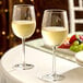 A pair of clear 16 oz. wine glasses filled with white wine on a table.