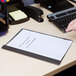 A hand types on a Universal Office black leatherette report cover on a clipboard.