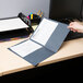 A person holding a dark blue Universal embossed paper pocket folder with papers inside.