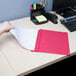 A person's hand using a red Universal Office report cover to hold a piece of paper.