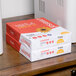 A stack of white boxes on a table containing Universal Office white 3-hole punched copy paper.