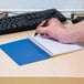 A hand holding a pen writing in a National Blue College Rule spiral notebook.