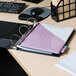 A black Universal economy non-stick view binder with a pink paper in it on a desk with a laptop and pen.