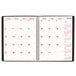 A white spiral bound Brownline Essential Collection 14-month planner with black and red text on the cover.