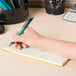 A hand holding a green pen writing in a Rediform Green Gregg Rule Spiral Steno Notebook.