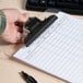 A hand holding a Universal clear plastic clipboard with paper and a pen.