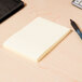 A Universal yellow lined self-stick note pad on a table with a pen.