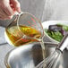 A person pouring Grapeola Grape Seed Oil into a bowl.