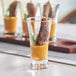 A tray of Acopa flared pilsner beer tasting glasses filled with meat and sauce on a table at a catering event.