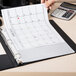 A hand using a Universal clear sheet protector to hold a calendar on a desk.