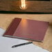 A Rediform burgundy visitor register book with a black pen on a table.