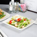 A Tuxton eggshell square china plate with salad on a table.