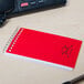 A red National wirebound memo book on a desk.