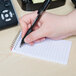 A hand holding a pen over a National Wirebound Narrow Rule Memo Book with assorted color covers.