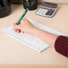 A hand using a green pen to write in a Mead spiral notebook.