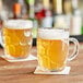 Two Acopa dimple beer mugs filled with beer on a table.