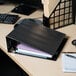 A black Universal economy view binder with papers and a pen on a desk.