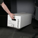 A person's arm holding a white Universal Economy Fiberboard storage box.