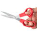 A hand holding a pair of Universal stainless steel scissors with red bent handles.