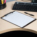 A Universal translucent black low profile plastic clipboard on a desk with a pen.