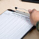 A hand holding a Universal translucent black low profile clip plastic clipboard with paper on it.