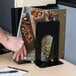 A hand using a black steel Universal economy bookend to hold a magazine on a table.