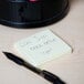 A yellow Universal self-stick note with writing next to a pen.