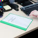 A person's hand holding a green Universal Office report cover with a clear cover and prong fasteners