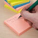 A hand writing with a pen on a Universal assorted neon color self-stick note.