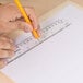 A person using a Universal clear acrylic plastic ruler to draw a pencil line.