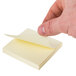 A hand holding a Universal yellow recycled sticky note.