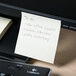 A yellow Universal sticky note with a note on it on a piece of paper.