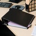 A black Universal non-view binder with papers on a desk.