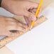 A person using a Universal wood ruler to measure with a pencil.