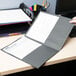 A person's hand holding a black Universal paper pocket folder with papers inside.