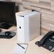 A white Universal economy view binder on a desk with a file folder and a phone.