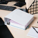 A white Universal economy view binder on a desk with a stack of books and a pen.