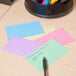 A table with Universal assorted color ruled index cards, a pen, and paper.