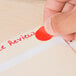 A hand holding a piece of paper with a red Avery neon red round label on it.