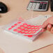 A hand using a red Avery neon label to put a sticker on a plastic container with red circles.