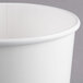 A close-up of a Huhtamaki white paper food cup with a lid on it.