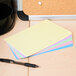 A stack of Universal assorted color ruled index cards on a table with a black pen and colorful papers.