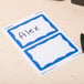 A white paper Universal name badge with a blue border and pen on a desk.